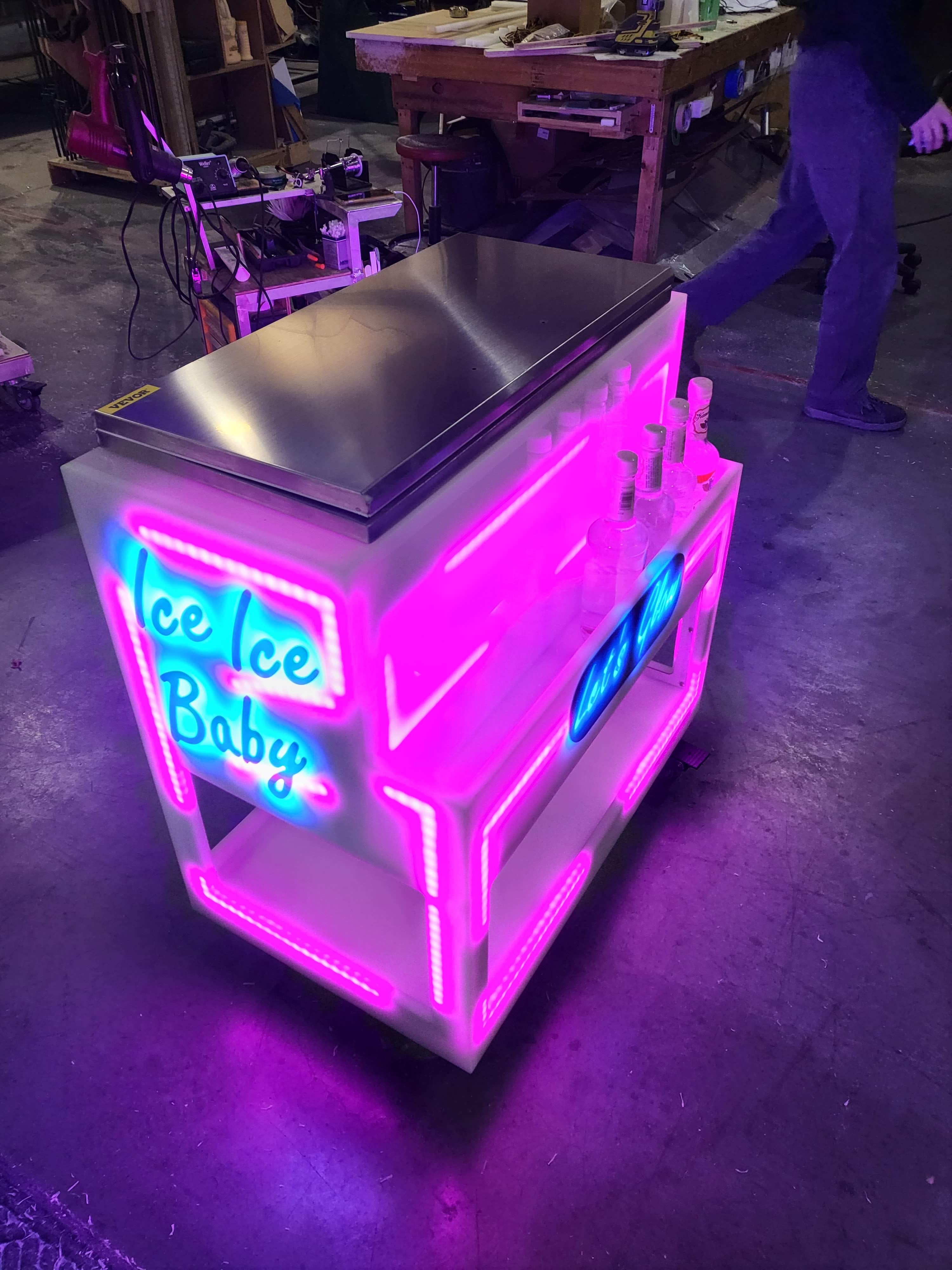 LED mini service cart and built in cooler in pink lighting with several liquor bottles.